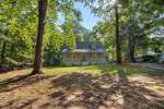 A light gray house at 112 Waiters Way in Youngsville, with a covered front porch, sits among tall trees, sunlight filtering through the leaves onto a spacious, partially shaded yard.