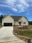 A new beige house at 35 Cotton Drive, Louisburg, features a two-car garage, concrete driveway, front steps, and a yellow caution tape across the yard under a blue sky.