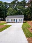 Charming small white house with blue shutters and a gray roof, seen from the front at 213 N Bickett Boulevard, Louisburg. A wide concrete driveway leads up to the entrance, surrounded by green grass and trees in the background.