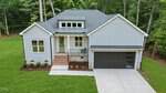 Modern gray house at 135 Seneca Drive, Louisburg, featuring a dark garage door, brick steps leading to a covered front porch, and surrounded by green lawn and trees.