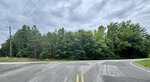 A cracked asphalt road meets 00 Ross Mill Road in front of dense green trees under a cloudy sky. Power lines and a utility pole are visible on the left side, hinting at the quiet surroundings of Henderson.