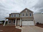 Two-story tan house with white trim, double garage, covered porch, and several windows located at 168 Sugarmaple Way, Youngsville. The driveway and walkway are surrounded by bare soil. The sky is overcast with gray clouds.