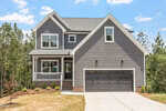 Charming two-story gray house with white trim located at 931 Woodland Road in Creedmoor. Featuring a welcoming front porch, an attached two-car garage, and a concrete driveway, this home offers both style and convenience. The yard includes minimal landscaping with small shrubs and brown grass, while mature trees provide a scenic backdrop.