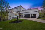 Modern white two-story house with a dark roof, large windows, three-car garage, and landscaped front yard at 543 Sagamore Drive in Louisburg, set against a twilight sky with trees and a lake in the background.