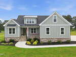A modern gray house with white trim, stone accents, and a covered front porch decorated with patriotic bunting sits proudly at 35 Wheatfield Lane in Youngsville. The yard is beautifully landscaped with shrubs and a curved sidewalk, all beneath a clear blue sky.