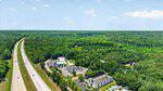 Aerial view of a highway running alongside a forested area near Tbd Zeb Robinson Road in Henderson, with a hotel and parking lot in the foreground and dense green trees stretching into the distance under a blue sky with scattered clouds.