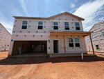A two-story house at 36 Plantation Drive in Youngsville is under construction, wrapped in a weather barrier with exposed framing. The front porch remains unfinished, and the ground is red dirt. Neighboring houses are also under construction under a sunny sky.