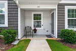 A small front porch with a single chair, potted plant, doormat, and house number 105. The house exterior is gray with white trim and surrounded by green bushes and grass.