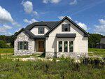A modern two-story house with stone and light siding, large windows, and a black roof sits on a grassy lot at 40 Wheatfield Lane in Louisburg, under a blue sky with scattered clouds.