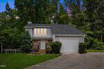 A two-story house with large windows, a single-car garage, and brick accents at 306 Smoke Tree Way, Louisburg, surrounded by green trees at dusk under a colorful sky.