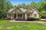 Single-story house with a front porch, beige siding, red shutters, and gabled roof located at 645 Timberlands Drive in Louisburg. Surrounded by a green lawn, shrubs, trees, and a cement walkway leading to the entrance.