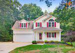 Two-story suburban house with a front porch, red shutters, and a two-car garage located at 30 Ridge Haven Drive in Louisburg. Surrounded by trees and shrubs, with a curved driveway and green front yard. Blue sky and some clouds overhead.