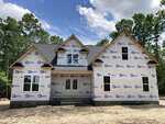 A two-story house under construction at 2154 Grove Hill Road in Franklinton, covered in white weatherproof wrap with logos, surrounded by trees and a dirt yard, under a partly cloudy sky.