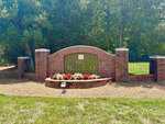 A brick sign with "Olde Brassfield" surrounded by red and white flowers, set against a backdrop of trees and green grass, marks the entrance to 3669 Brooks Bend in charming Franklinton.