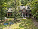 Two-story brick house with white trim, black shutters, and a covered front porch, surrounded by trees and greenery. Two blue kiddie pools are on the lawn in the foreground.