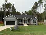 Single-story gray house with black roof, white trim, stone accents, and a black garage door located at 30 Lemon Drop Lane in Franklinton. There's a large rock in the front yard, surrounded by grass and tall trees in the background.