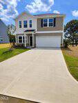 Two-story beige and white house with black shutters, double garage, and a long, clean concrete driveway located at 165 Spotted Bee Way in Youngsville. Green grass and a few young trees surround the house under a partly cloudy sky.