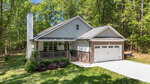 A single-story house at 111 Nashua Drive, Louisburg, featuring a front porch, white siding, brick accents, and a two-car garage, is nestled amid green grass and trees under a clear sky.