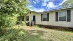 Single-story manufactured home at 4552 Gray Rock Road in Kittrell with beige siding, black shutters, and a blue front door. The house is surrounded by overgrown grass and trees, with a small porch and steps leading to the entrance under a partly cloudy sky.