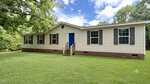Charming single-story beige house with black shutters, a blue front door, and a small porch with steps at 4552 Gray Rock Road. This Kittrell home is surrounded by green grass, mature trees, and set beneath a partly cloudy sky.