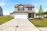 Two-story beige house with a white garage door, dark shutters, and a small covered entrance welcomes you to 111 Hybrid Street in Oxford. A concrete driveway and walkway lead to the front of the home. The lawn is green, accented by a young tree on the right side, all illuminated by a bright, sunny day.