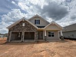 A new two-story house with a stone and siding exterior, double garage, and covered porch sits on a dirt lot under a partly cloudy sky in Youngsville at 85 Moon Flower Walk.