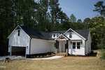 A white single-story house with black roof and trim at 1316 Sagamore Drive, Louisburg, features an attached two-car garage, a front porch with columns, and a landscaped yard surrounded by tall trees and greenery.