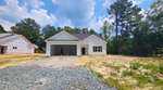 A newly constructed white house at 101 Hawthorn Street in Louisburg, with an open garage, sits on a lot with gravel and patches of grass, surrounded by trees and a partly cloudy sky. Another house under construction is visible to the left.