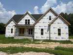 A partially constructed house with house wrap, black roof shingles, unfinished yard, and a covered front porch sits on Lot 4b Flat Rock Road in Franklinton, set against a partly cloudy sky and treeline in the background.