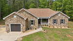 Nestled at 490 Shawnee Drive, Louisburg, this single-story stone house features a brown roof, attached garage, black shutters, and a small front porch. Surrounded by trees and landscaped with rocks and mulch, this charming home offers both curb appeal and tranquility.