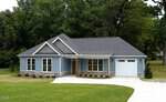 A single-story blue house with a gray roof, white trim, and an attached garage sits on a green lawn with a curved driveway at 308 S Elm Street in Creedmoor, surrounded by tall trees and dense greenery in the background.