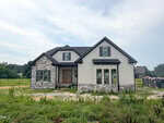 A modern house with stone and beige siding sits on a grassy lot at 40 Wheatfield Lane in Louisburg, featuring multiple front-facing gables and large windows. Construction materials are visible to the right.