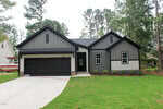 Modern single-story house at 209 Sequoia Drive in Louisburg, featuring a sleek gray and black exterior, a spacious driveway, two-car garage, green lawn, and trees in the background.