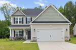 Two-story suburban house with gray siding, black shutters, a white garage door, and a covered front porch. Located at 520 Husketh Road in Youngsville, this home is set on a green lawn with trees in the background and a clear sky overhead.