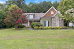 Charming single-story house with stone and green siding located at 2117 Olde Brassfield Drive, Franklinton. Featuring a welcoming front porch, gabled roof, blooming trees, and a large manicured lawn, this home is surrounded by tall trees and lush greenery in a quiet suburban setting.