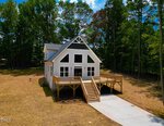A modern white two-story house with large windows, a triangular roof, and a spacious wooden deck sits at 117 Friendly Lane in Henderson. Set on a cleared lot surrounded by tall green trees, the home features a concrete driveway that leads up to the inviting front steps.