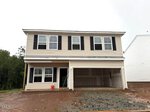 A two-story beige house with black shutters is situated at 33 Plantation Drive, Youngsville. Featuring an unfinished yard and an open two-car garage, the home has windows already installed, though the driveway and landscaping remain incomplete.