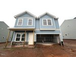 A newly constructed two-story blue house with white trim, a covered porch, double garage, and bare front yard awaits you at 45 Plantation Drive in Youngsville. The garage door is open, revealing the unfinished interior of this charming home.