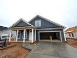 A newly built blue house with white trim at 84 Moon Flower Walk, Youngsville, features a covered front porch, double garage, and unfinished yard. The driveway and sidewalks are concrete. Another house under construction is visible on the right.