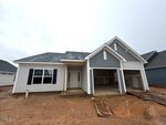 Single-story house under construction at 88 Moon Flower Walk in Youngsville, featuring gray siding, a two-car garage, white trim, black shutters, and a covered entry. The ground is muddy, and construction materials are scattered in front of the garage.