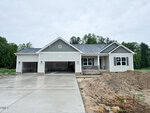 Single-story house with gray siding, a covered front porch, and a three-car garage located at 55 Kettle Creek Drive in Zebulon. Fresh concrete driveway and some exposed dirt in the foreground. Trees and cloudy sky in the background.
