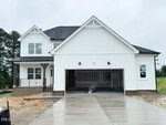 A two-story white house with black roof shingles sits at 10 Diamond Creek Drive, Zebulon. It features an attached double garage and unfinished landscaping. A person is kneeling on the garage floor, while the driveway appears freshly poured and wet.