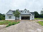 A newly constructed, light blue house with white trim, double garage, and unfinished landscaping is located at 35 Torrent Lane in Zebulon. The driveway is gravel, and a small tree stands in front of the house. The sky is overcast.