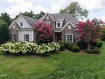 Two-story suburban house with stone and siding exterior, located at 693 Hawthorne Place in Creedmoor, surrounded by green lawn, bushes, blooming white and pink-flowered trees, and trees in the background under a partly cloudy sky.