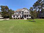 Situated at 8808 Sprouted Lane in Wake Forest, this two-story suburban house features gray siding with white trim and elegant stone accents. The home boasts a covered front porch, manicured bushes, and a large, neatly mowed front lawn dotted with trees and complemented by a driveway on the left side.