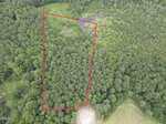 Aerial view of a wooded area with a dirt clearing at the bottom near 2 Hidden Dreams Way Road, Zebulon. The land is outlined in red, clearly showing boundaries. A small pond and marshy area are visible near the top, and dense forest surrounds the outlined plot.