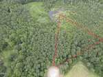 Aerial view of a forested area along 3 Hidden Dreams Way Road, Zebulon, with a triangular section outlined in red. There is a round cleared area at the bottom of the outlined section and a pond surrounded by trees near the top of the image.