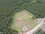 Aerial view of a partially cleared grassy field bordered by dense trees, with a section outlined in red near 4 Hidden Dreams Way Road in Zebulon. A dirt road runs alongside the field, and some cleared patches and debris are visible near the road.