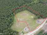 Aerial view of a forested area in Zebulon with a cleared grassy plot outlined in red. The plot, located off 5 Hidden Dreams Way Road, is bordered by trees on most sides and a dirt road along one edge. Some construction materials or debris are visible near the road.
