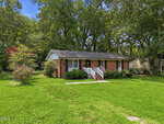 Charming single-story red brick house with white trim, black shutters, and a welcoming front porch with railings. Nestled on a large grassy lawn at 303 Sunset Avenue in Oxford, this home is surrounded by mature trees under a clear blue sky.
